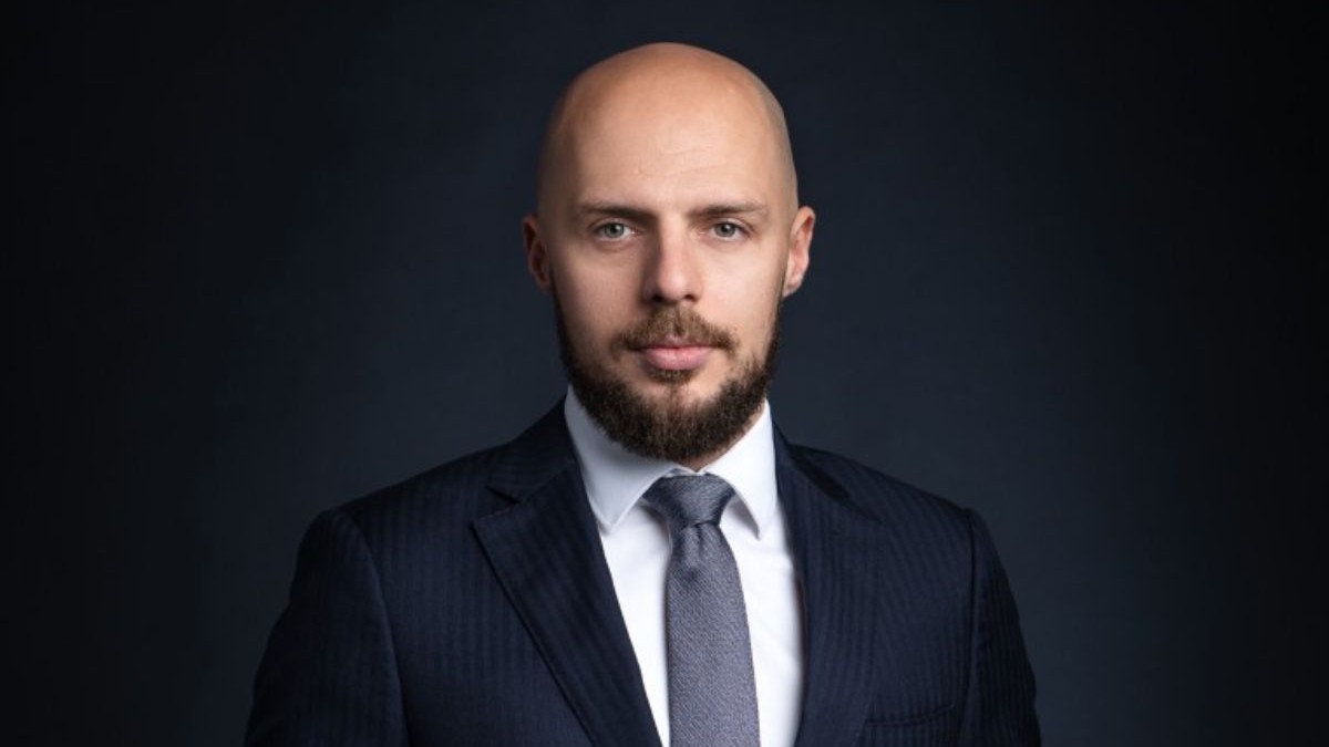 Cristian Pelivan, directorul executiv ARMO, îmbrăcat în costum negru, cu cămașă albă și cravată gri, pe un fundal negru