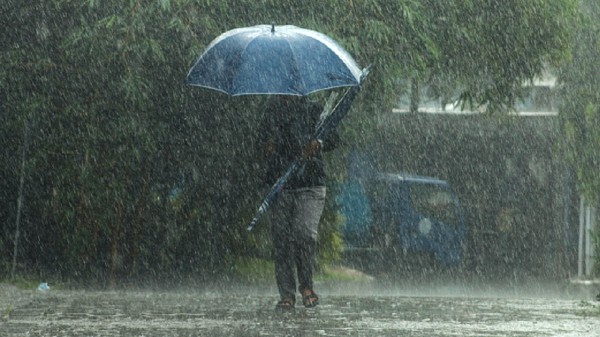Imaginea surprinde o persoană care înaintează cu greu printr-o ploaie torențială pe stradă, protejându-se cu o umbrelă albastră sub un cer întunecat.