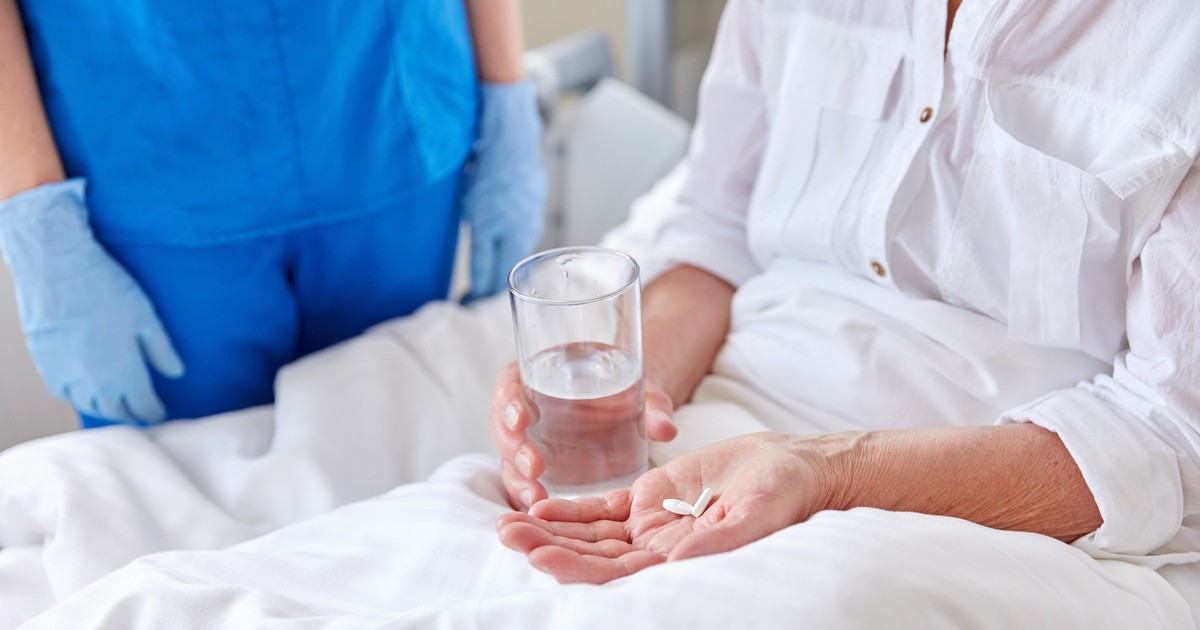 femeie pe patul de spital ia medicamente. Foto: Shutterstock