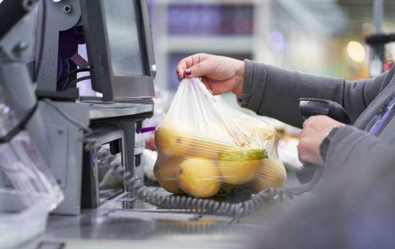 O casieră care scanează o pungă din plastic plină cu lămâi la casa de marcat a unui magazin sau supermarket.   