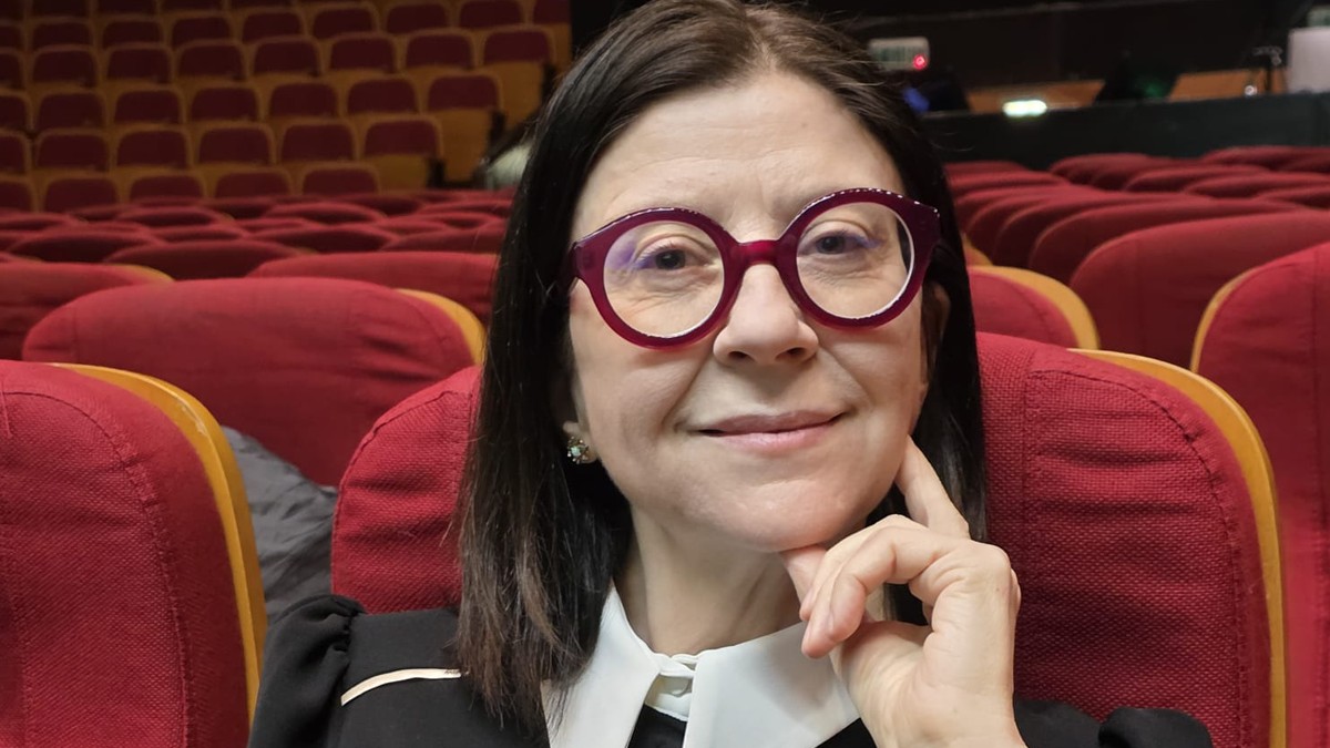 Andreea Chiș cu mâna în bărbie, zîmbește în timp ce stă pe un scaun într-o sală de conferință goală.