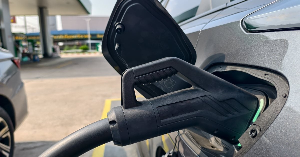 Un cablu cu conector introdus în portul de alimentare al unui vehicul electric gri, parcat într-o stație de încărcare.
