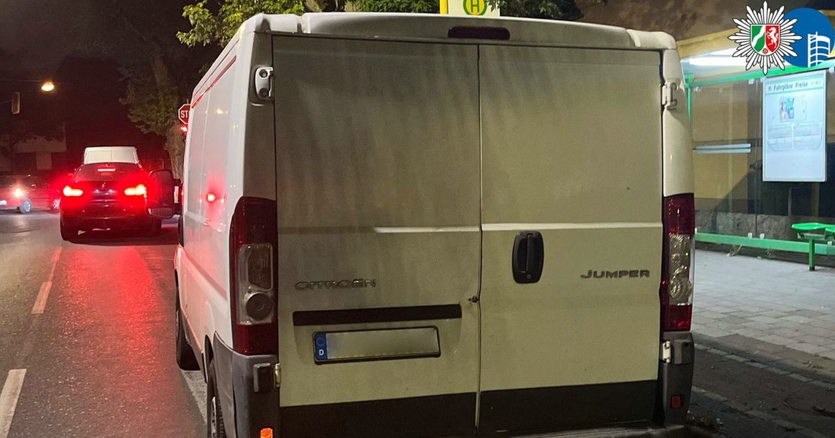 O mașină dubiță albă, fotografiată cu spatele și numărul de înmatriculare blurat, parcată pe o stradă din Germania, iar în fața ei se vede o mașină neagră cu farurile aprinse