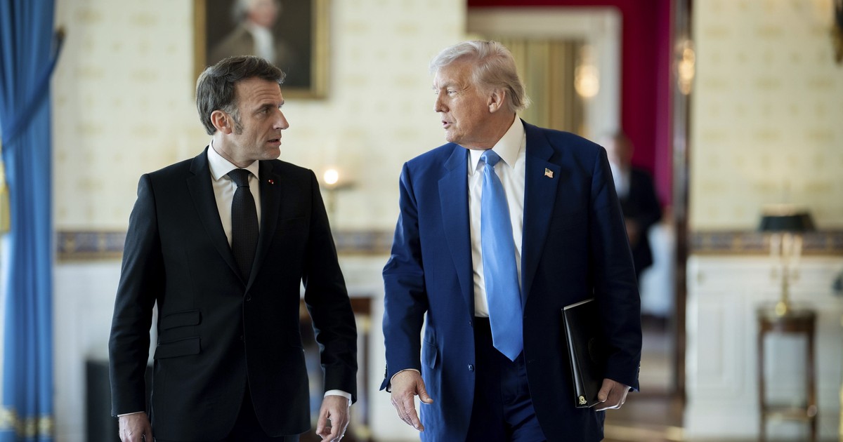 Emmanuel Macron (stânga) și Donald Trump (dreapta) surprinși în timp ce vorbesc. Președintele francez poartă un costum negru, cu o cămașă albă și cravată neagră, iar președintele SUA poartă unul albastru. Liderul american are cămașă albă și o cravată albastru deschis. Imaginea a fost făcută în februarie 2025