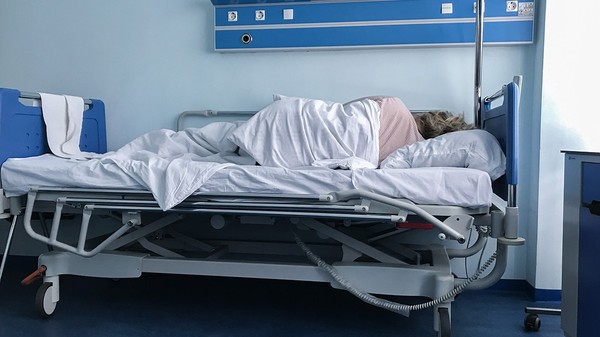 O femeie cu spatele într-un pat din spital