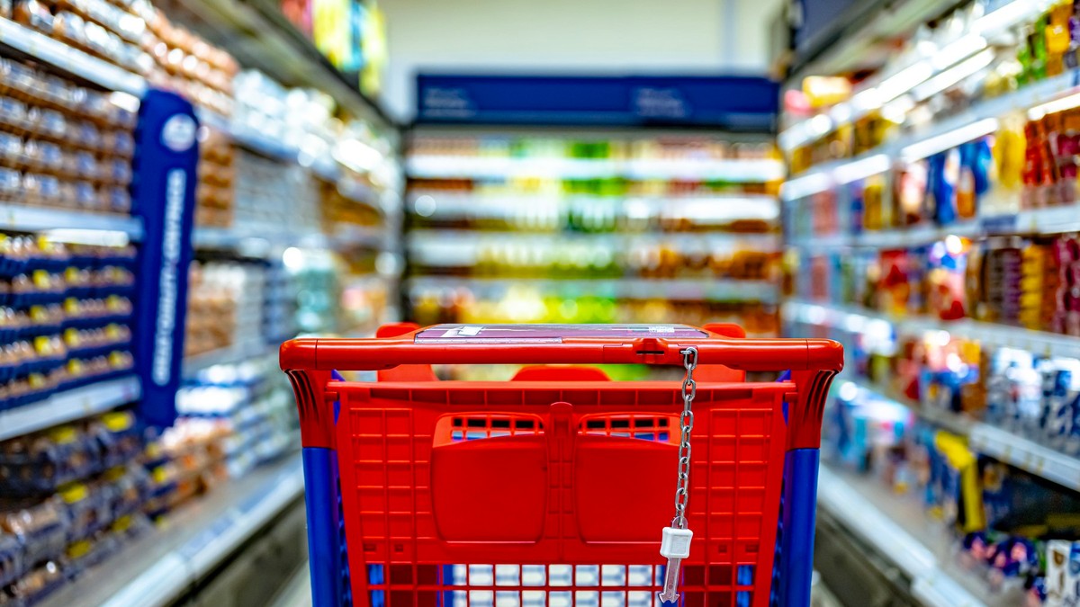 Un coș de cumpărături roșu se vede pe culoarul unui supermarket