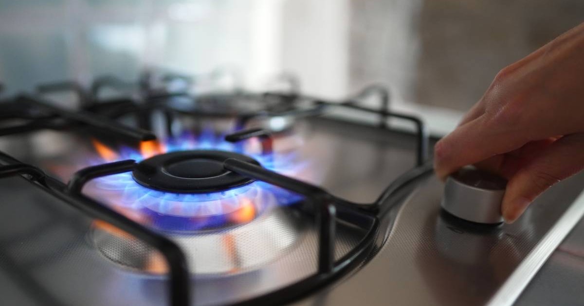 O mână de femeie care apasă și rotește butonul unui aragaz pe gaz, flacăra se aprinde la ochiul aragazului gri