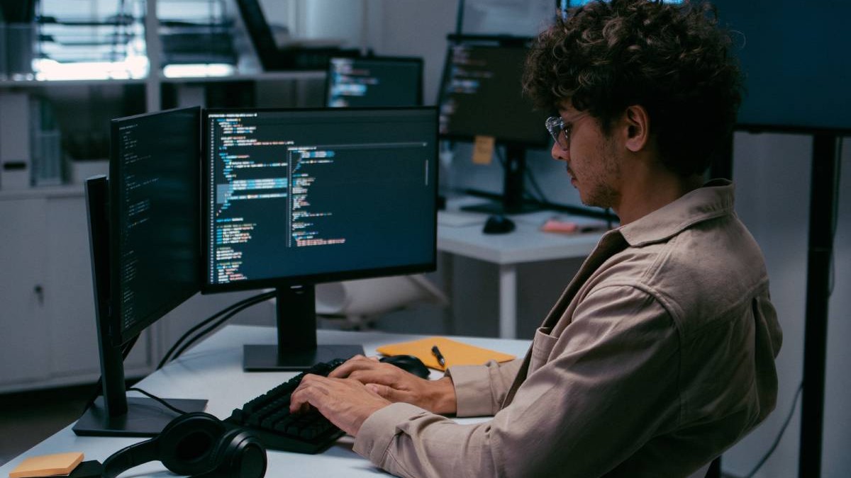 dezvoltator de software care lucrează pe computer desktop, care se uită la site-urile de ecran la locul de muncă de birou.