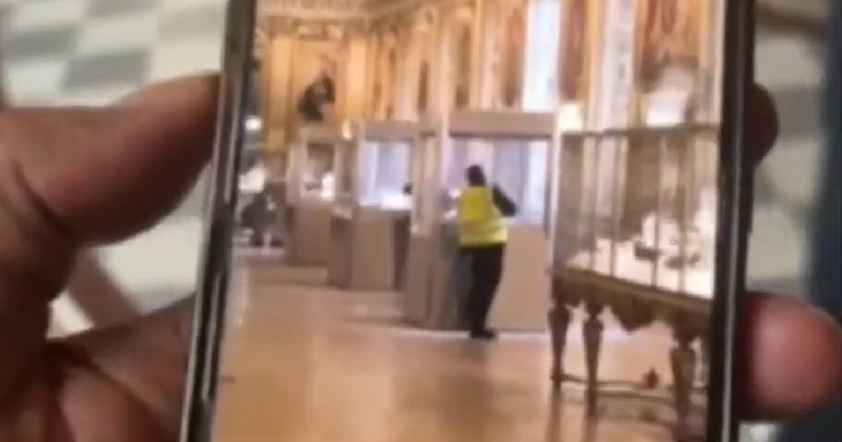Imaginea surprinde un bărbat purtând o vestă galbenă lângă o vitrină, în Galeria Apollon din Muzeul Luvru