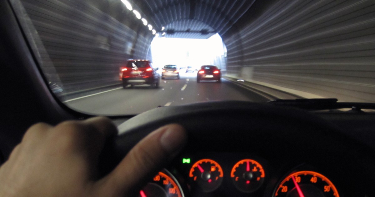 Perspectiva șoferului din interiorul unei mașini aflându-se la volan, în timp ce se deplasează printr-un tunel rutier în direcția ieșirii, în spatele altor mașini.
