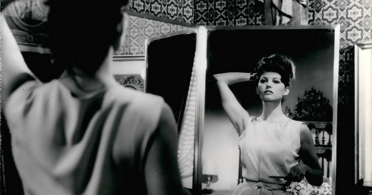 Claudia Cardinale in 1961 in filmul „Lions Get Loose”. Actrita, imbracata intr-o rochie fara manesci se priveste intr-o oglinda intr-o scena din film