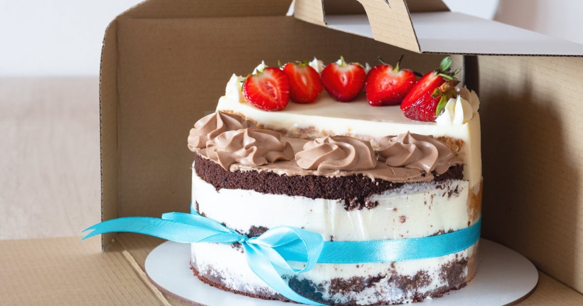 Un tort de vanilie cu ciocolată și frișcă, decorat u căpșuni și pus într-o cutie de carton