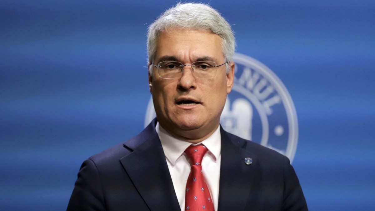 Ministrul interimar la Muncii, Dragoș Pîslaru, îmbrăcat la costum și cu ochelari, vorbește la o conferință de presă, iar în spate are un fundal albastru, București, ianuarie 2026