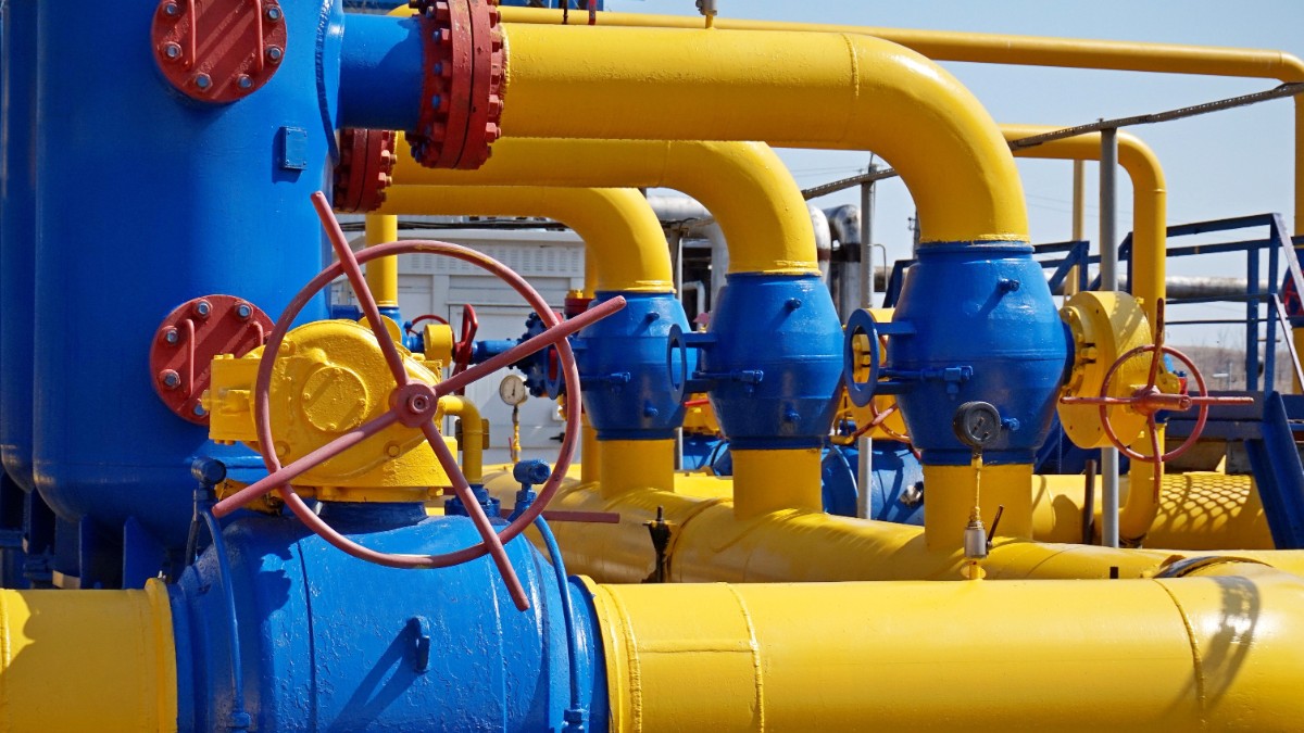 O instalație industrială de gaze este alcătuită din conducte groase galbene și componente metalice albastre, conectate prin valve și robinete. Echipamentele sunt parte dintr-un sistem de distribuție sau reglare a presiunii gazului, într-un cadru tehnic bine organizat.