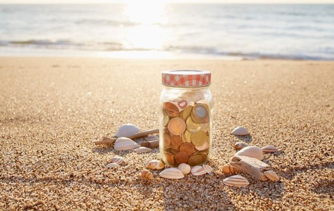 Bancnote și monede euro într-un borcan pe plajă, la apusul soarelui 