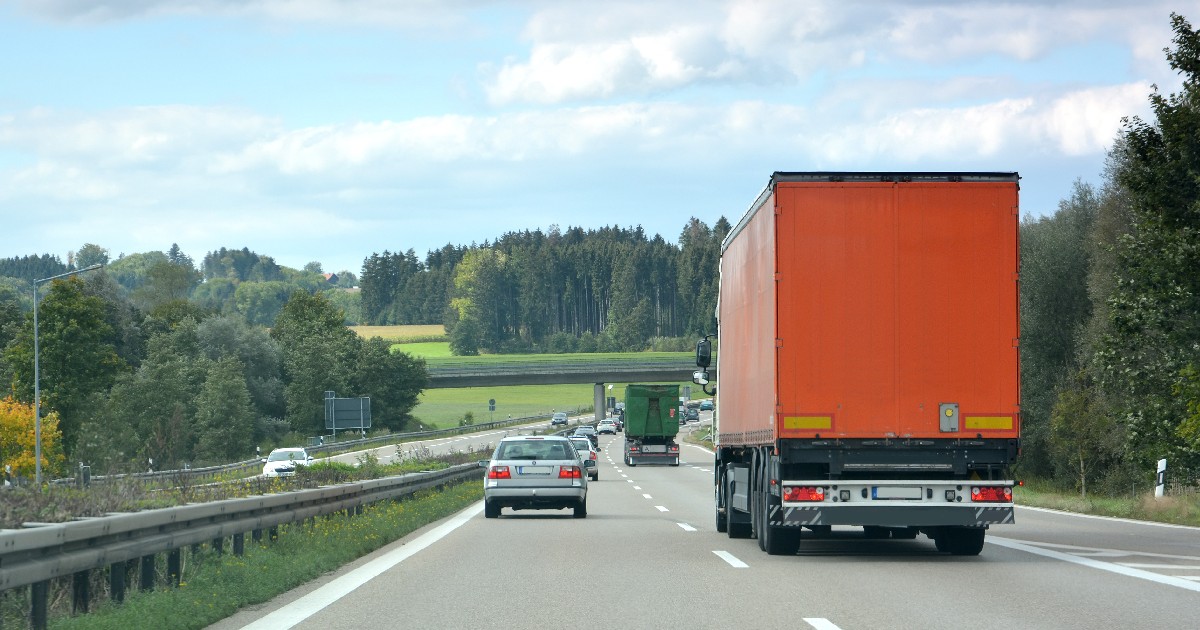 o autostradă din Austria, cu mașini și camioane circulând pe un drum drept, copaci și dealuri verzi sub un cer parțial înnorat.