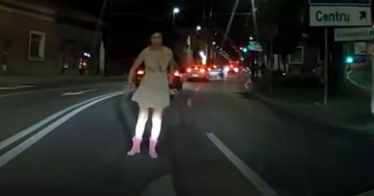 Tânăra din Cluj, îmbrăcată cu un palton crem decoltat și cizme roz de cowboy, pe mijlocul unei străzi, în fața unei mașini