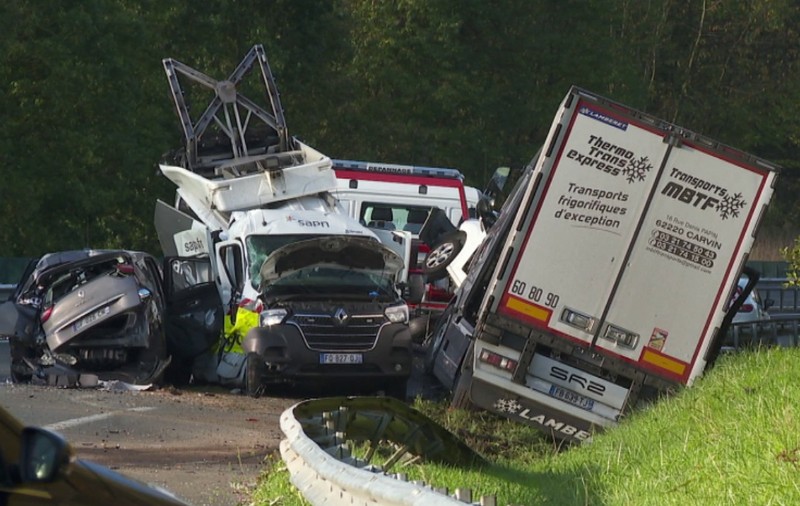 Locul unui accident rutier grav pe o autostradă, implicând un camion frigorific înclinat în șanț și mai multe vehicule utilitare și autoturisme puternic avariate.