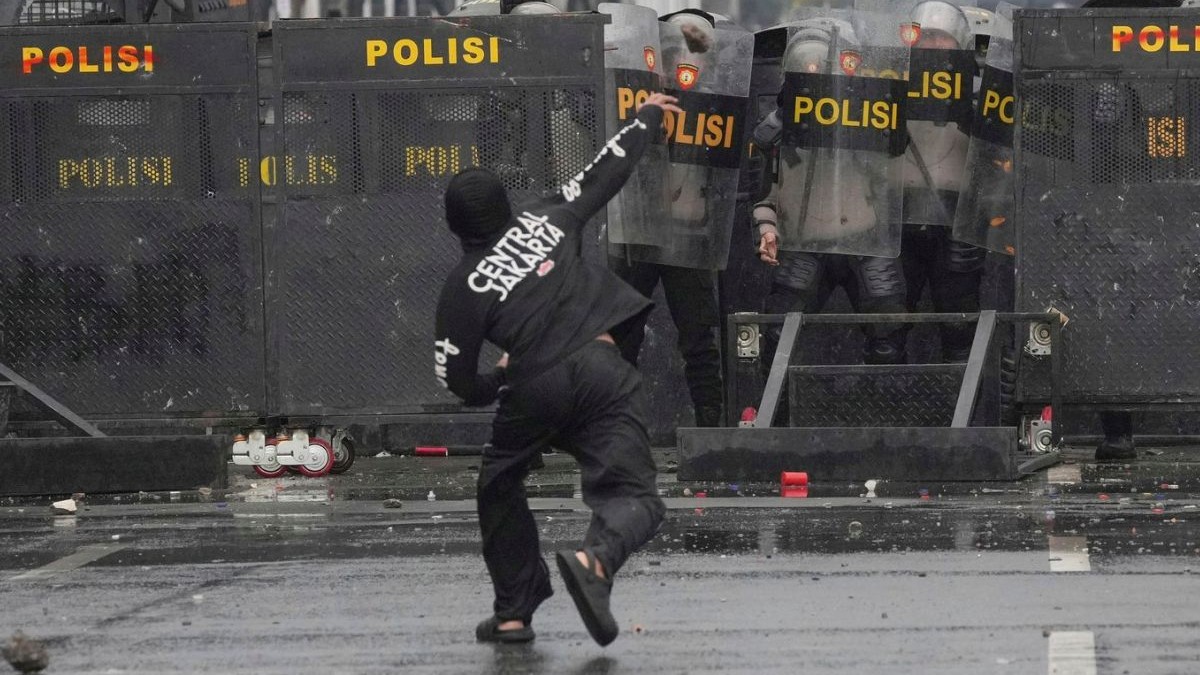 Polițiștii se protejează cu scuturi anti-revoltă în timp ce un protestatar aruncă cu pietre în ei în timpul unei manifestații împotriva alocațiilor generoase acordate membrilor parlamentului, în fața parlamentului din Jakarta, Indonezia, duminică, 31 august 2025.
