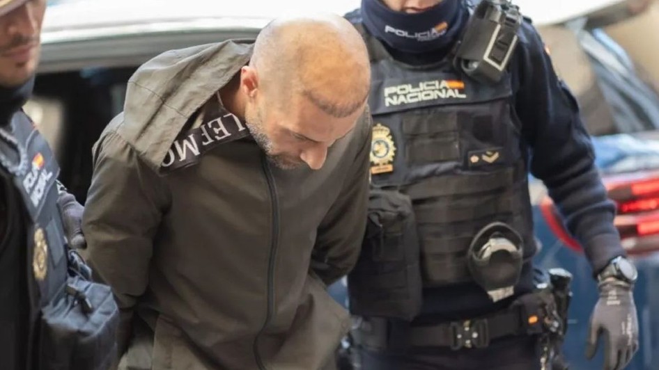 Un bărbat într-o jachetă gri, încătușat, este escortat de doi polițiști