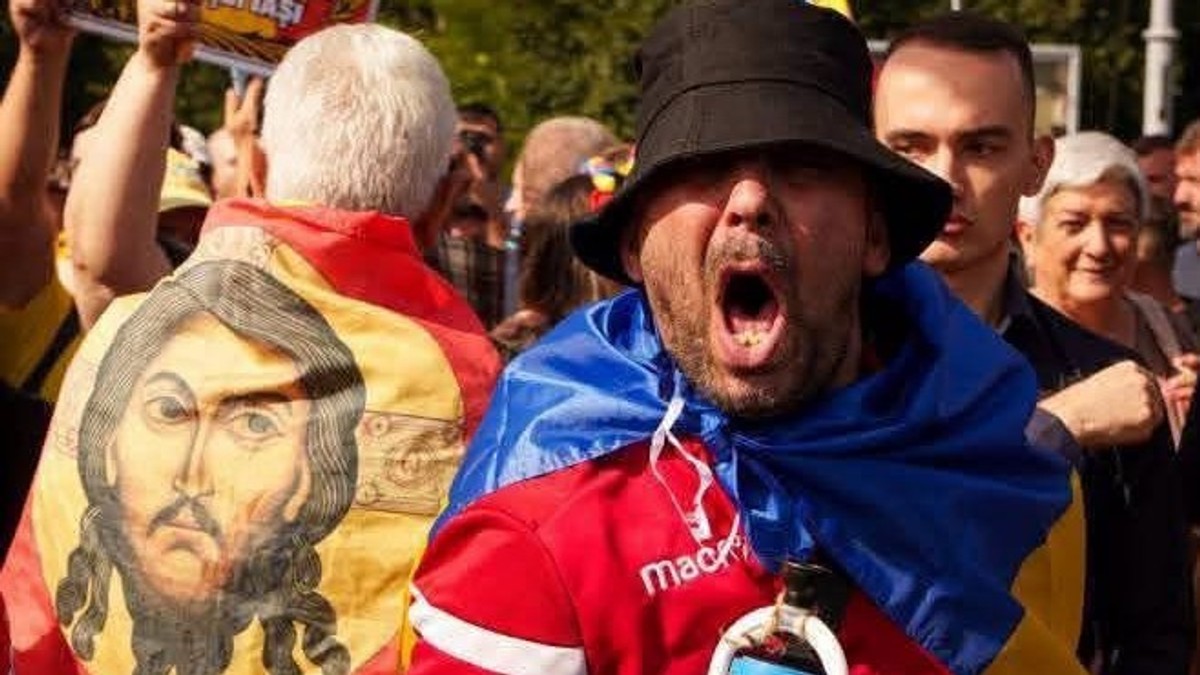 O imagine cu fața lui Isus pe un steag purtat pe spate de un protestatar, langa un al protestatar care tip la protestul fermierilor din Piața Victoriei, de pe 15 septembrie
