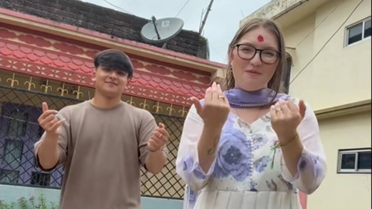 Nepalezul care lucrează în România și soția română, în Nepal, în timp ce dansează pe manele în fața casei. Ea poartă o rochie irațională albă cu flori mov, în timp ce el are un tricou maro