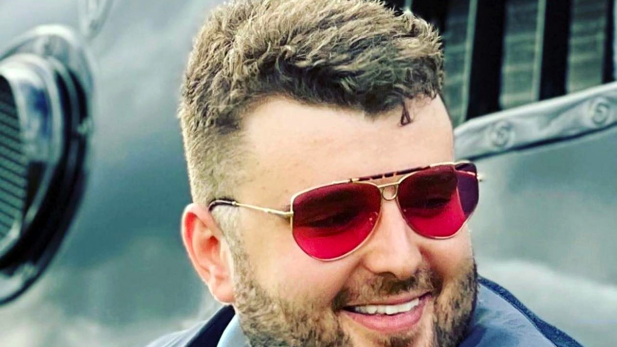 prim plan cu Victor Micula, purtând ochelari de soare cu lentile roșii, o cămașă și un sacou, zâmbind