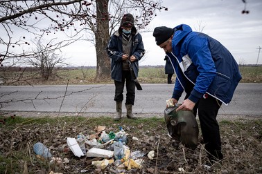 Doi dintre asistaţii social adună gunoiul de pe marginea drumului judeţean