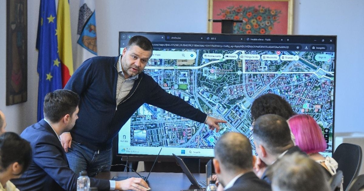 Ciprian Ciucu, primarul general al Capitalei, îmbrăcat cu blugi și pulover, arată cu mâna la un televizor pe care se vede o hartă, în timpul unei ședințe la Primăria București
