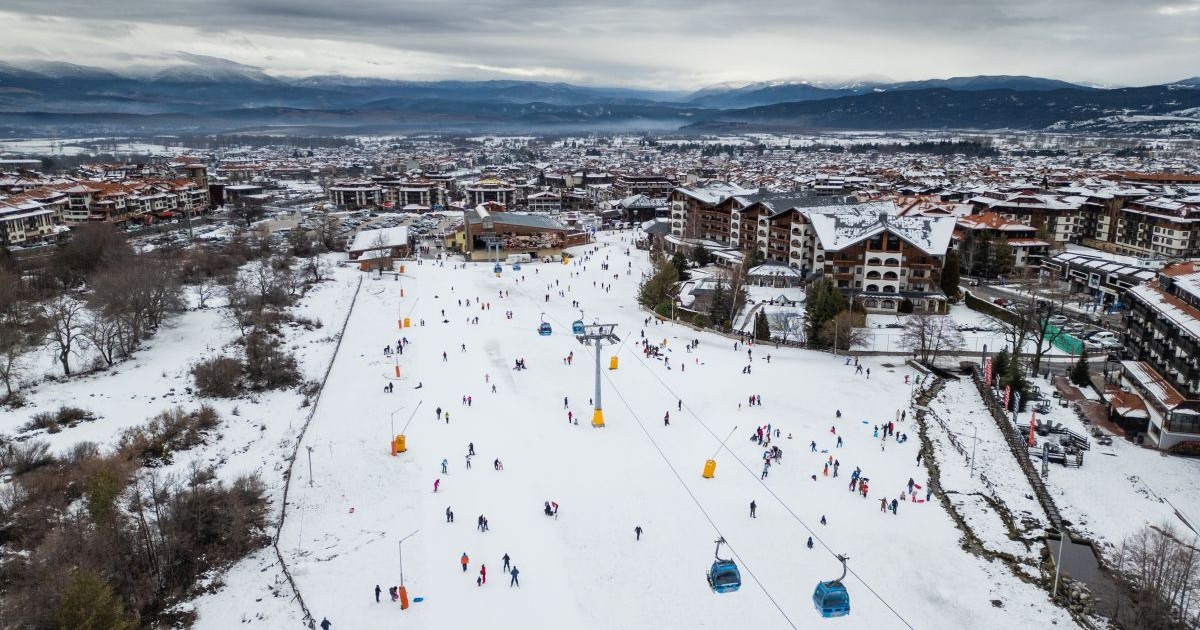 Schiorii se bucură de o zi cu zăpadă la stațiunea montană în timpul iernii, cu priveliști pitorești asupra orașului, Bansko, Bulgaria