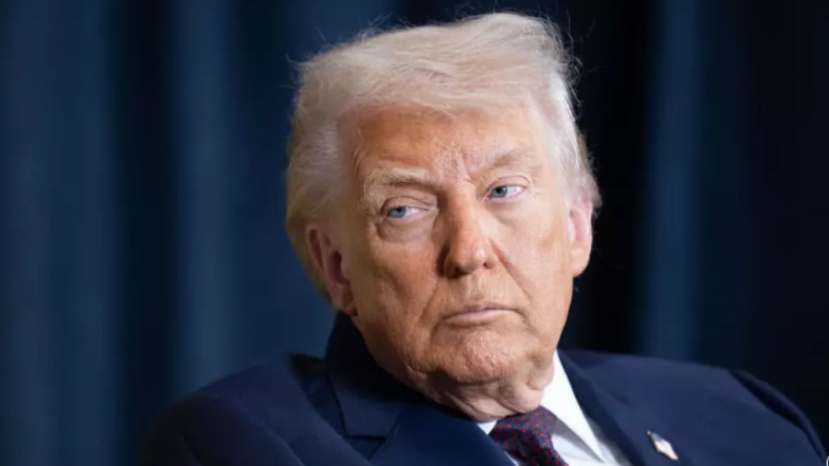 Donald Trump într-un sacou albastru închis în timp ce stă jos și privește în lateral.