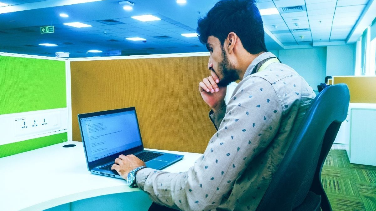 Imaginea surprinde un tânăr concentrat la locul de muncă dintr-un birou, stând la un computer.