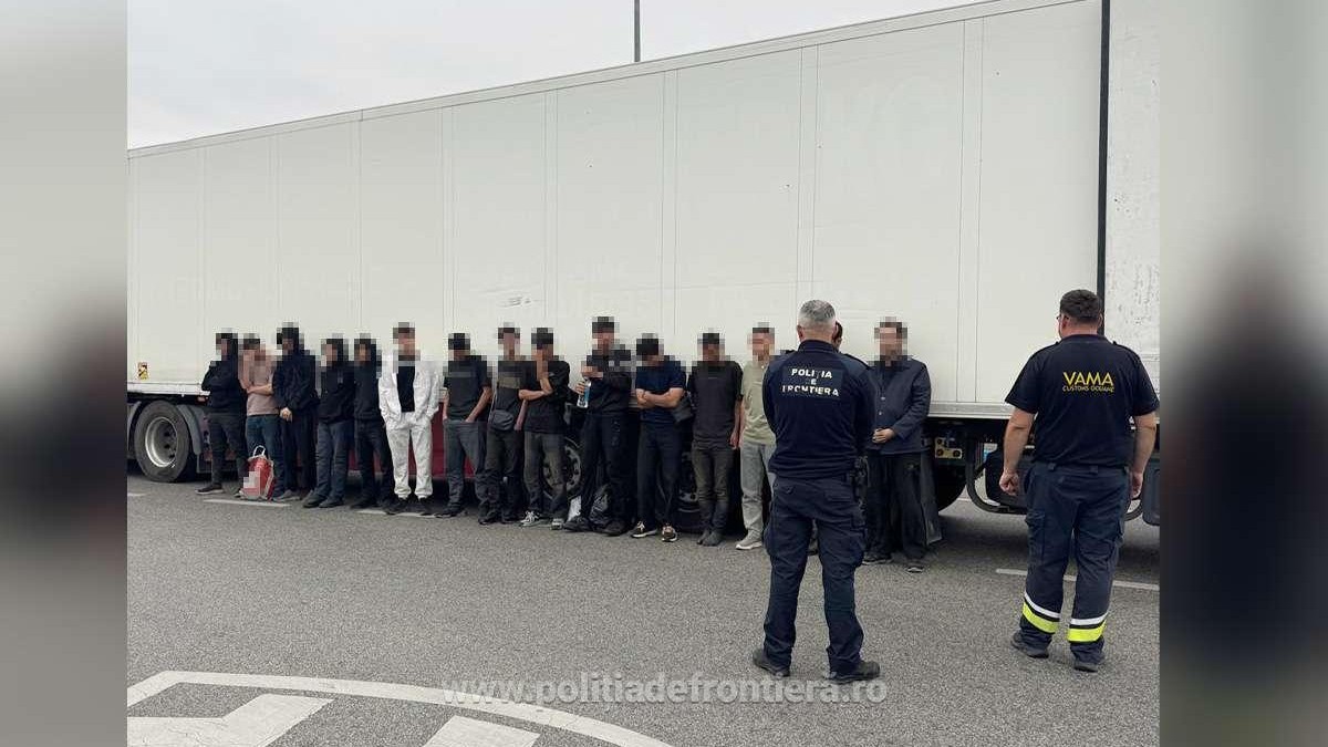 15 migranți din Irak stau aliniați în fața unui zid, supravegheați de polițiști de frontieră, la punctul de trecere a frontierei Calafat, 28 august 2026
