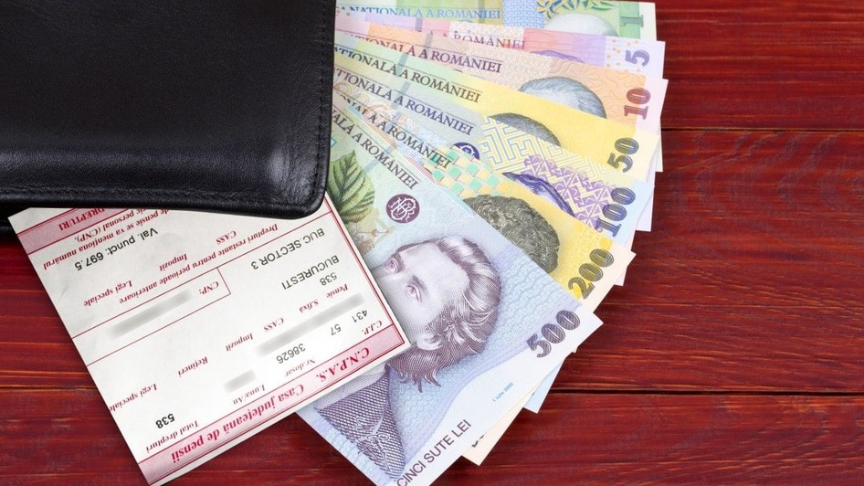 Mai multe bancnote românești ies dintr-un portofel al cărui colț negru se vede pe o masă, iar deasupra banilor este un cupon de pensie