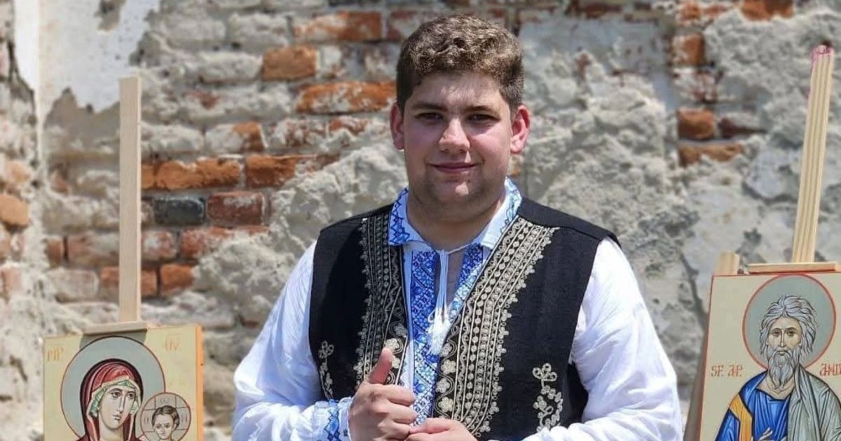Liviu Dobre, un tânăr care a murit lovit de fulger în timp ce cânta la vioară, imbrăcat în costum tradițional popular, cu ie si ilic, in fața unui perete din cărămidă cu icoane pictate