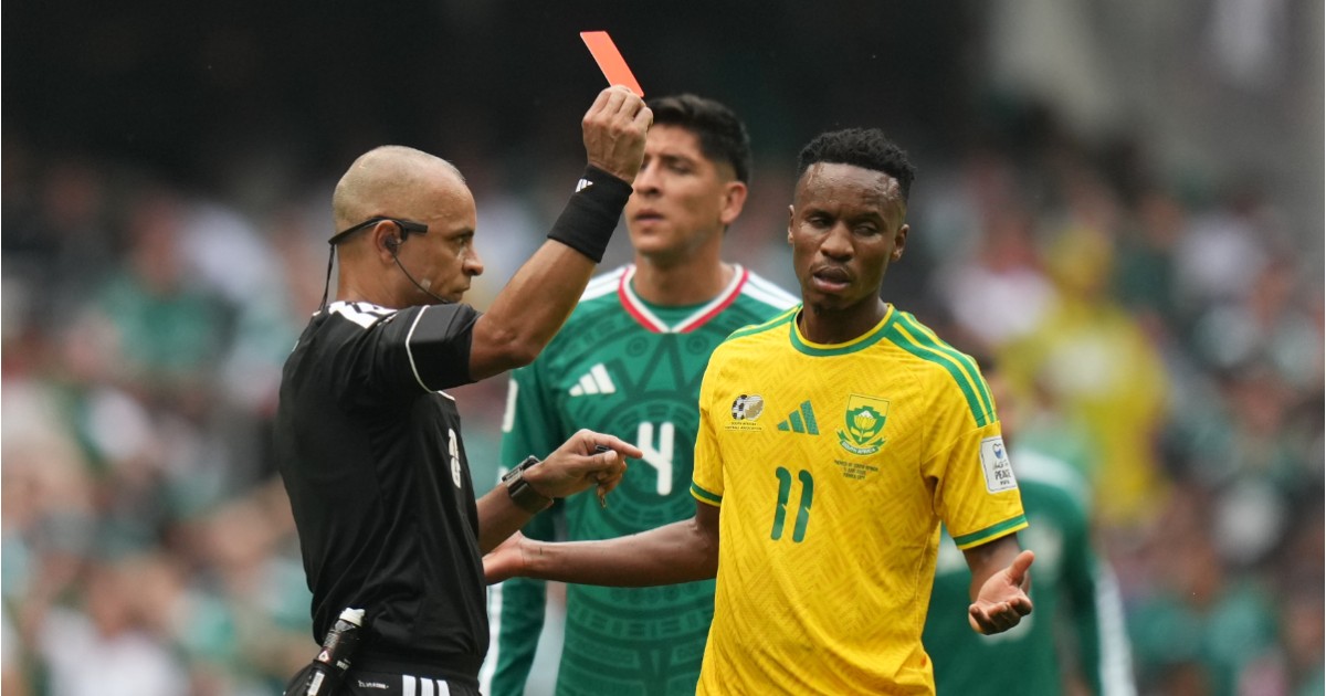 Themba Zwane în tricou galben, pe terenul de fotbal, confuz. Lângă acesta se află Wilton Sampaio cu un cartonaș roșu.