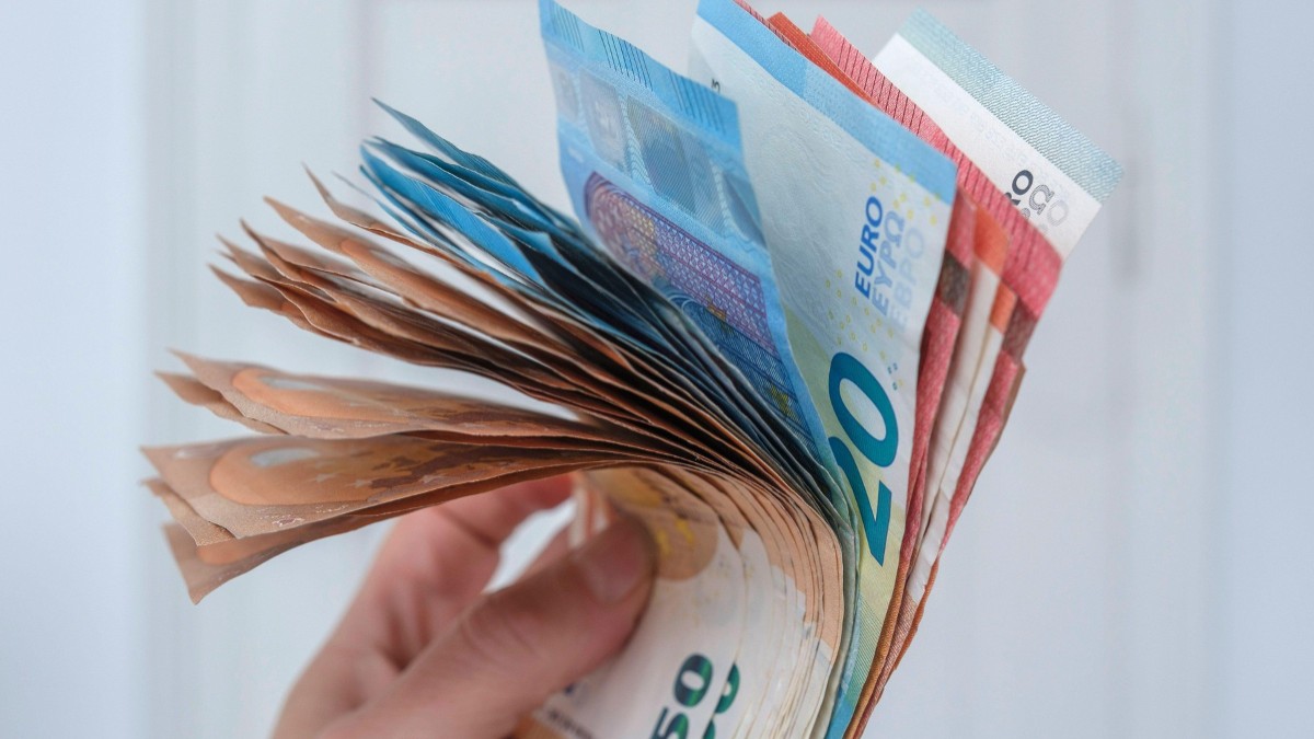 O persoană care ține bancnote de euro în mână