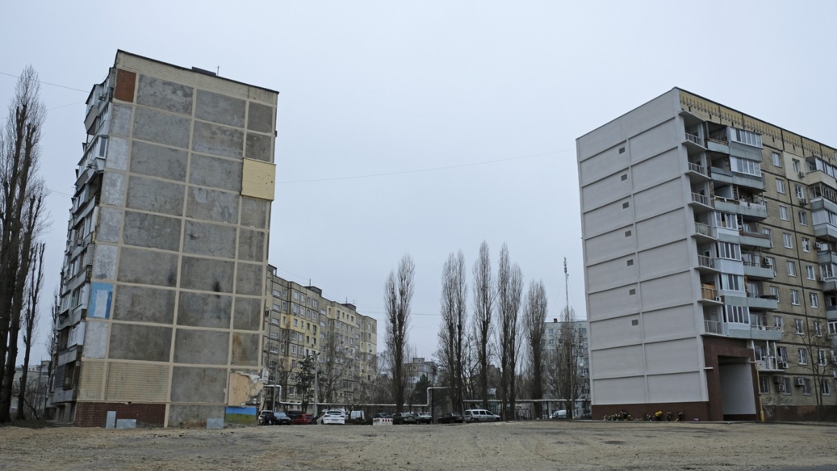 Imaginea surprinde un cartier rezidențial cu blocuri de apartamente vechi, într-o zonă urbană cenușie, cu copaci desfrunziți și spații largi, goale, sugerând sezonul rece. Atmosfera este rece și apăsătoare, reflectând lipsa de viață și dificultățile cu care se confruntă locuitorii din zonă.