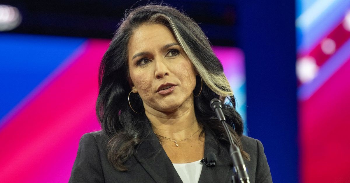Tulsi Gabbard, îmbăcată într-un taior negru și cu o bluză albă, vobește în fața unui microfon la o conferință de presă, februarie 2024