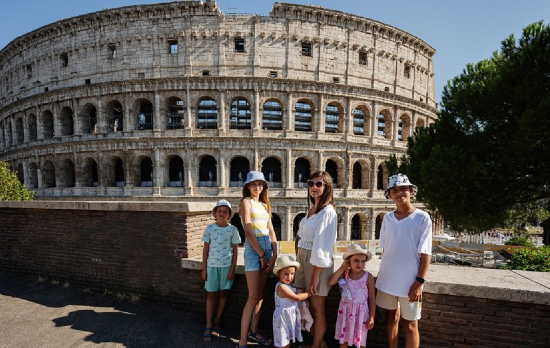 O mamă cu cinci copii pozează având Colosseumul ca fundal, în centrul istoric al orașului Roma, Italia.