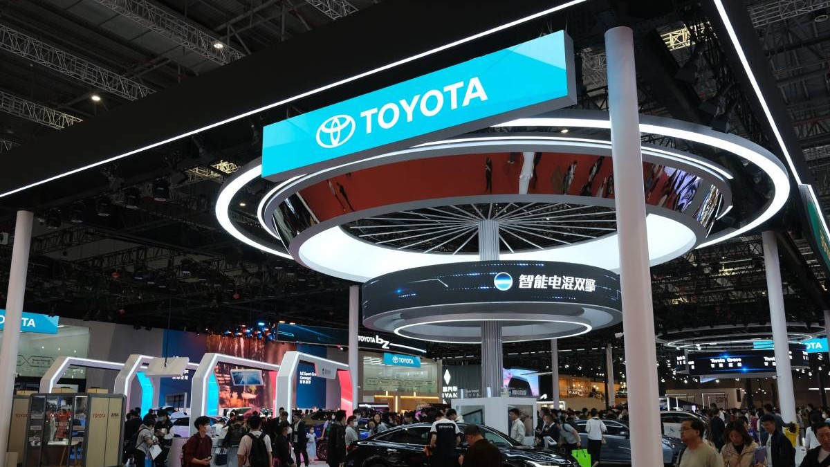 Stand al companiei Toyota la un târg internațional auto din China cu ecrane LED care afișează logo-ul Toyota și mesaje în limba chineză. În mijlocul standului se află o mașină neagră de prezentare