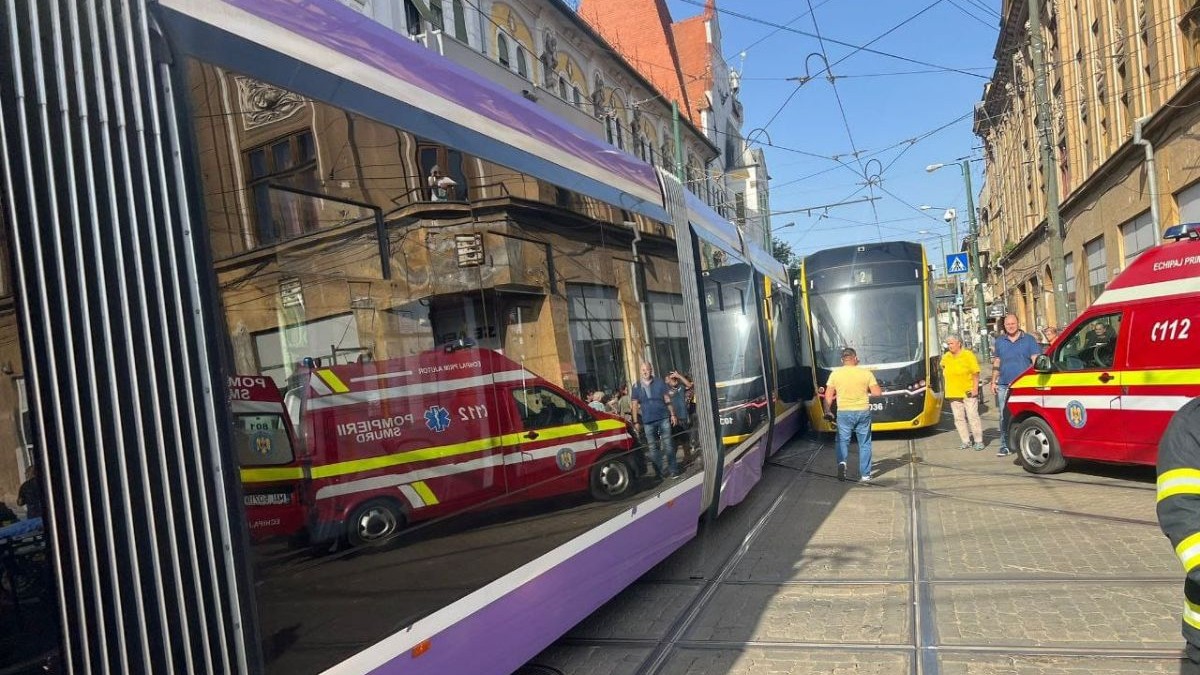 un tramvai mov și unul galben, lipite unul de celălalt după ce unul dintre ele a deraiat de pe șine, în Piața Traian, Timișoara. în jurul tramvaielor să văd mai multe autospeciale de salvare tip ambulanța, dar și oameni în haine civile