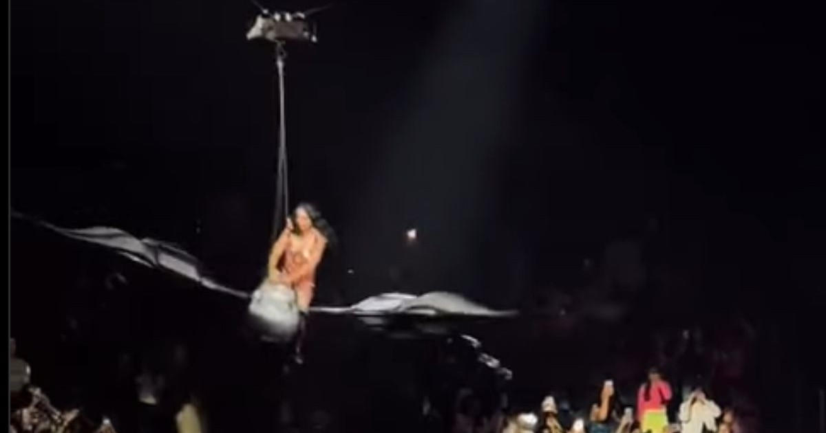 Katy Perry, îmbrăcată într-un body roșu cu pietre aplicate pe bust, stând în șezut pe un aparat zburător în formă de fluture în timpul unui concert în San Francisco, iulie 2025