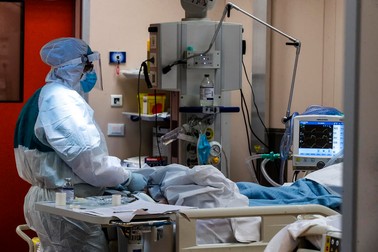O asistentă medicală îmbrăcată în echipament de protecție, alături de un pacient internat la Terapie Intensivă, într-un spital din Italia | Foto: EPA