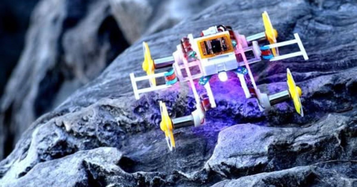 Un micro-robot care se aseamănă unei piese Lego, pe un fundal de rocă gri-albastră.
