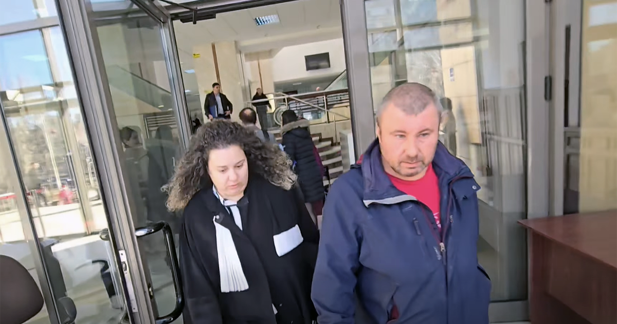 Un barbat imbracat intr-o geaca bleumarin si tricou rosu iese din tribunal alaturi de o avocata imbracata in roba neagra cu esarfa alba