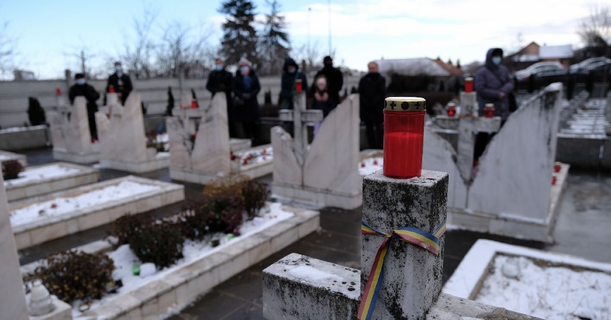 Persoane participa la ceremoniile dedicate comemorarii victimelor evenimentelor din Decembrie 1989, in Cimitirul Eroilor din Cluj, marti, 21 decembrie 2021. O lumânare rosie se vede in prim plan, pe un stalp de care este legat un tricolor.