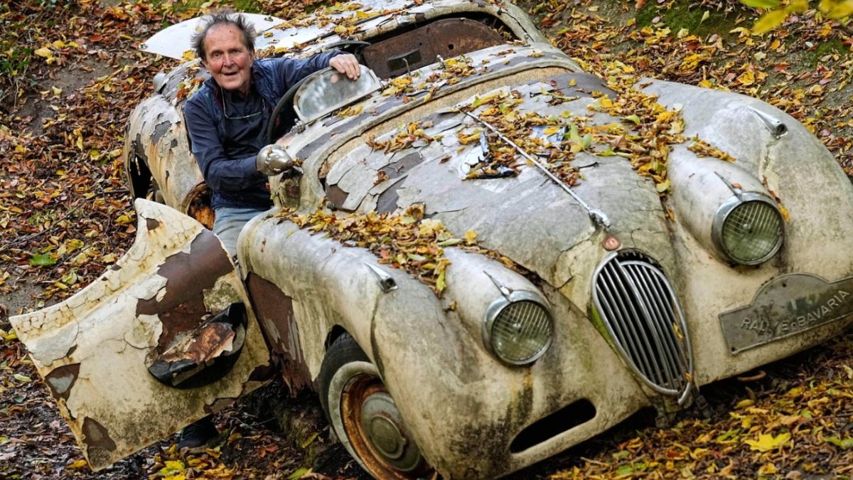 Colecționarul german de mașini Michael Fröhlich la volanul unui Jaguar clasic, într-o pădure, toamna, iar frunzele galbene au căzut pe mașina, vopsea este sărită și autoturismul are pete de rugină