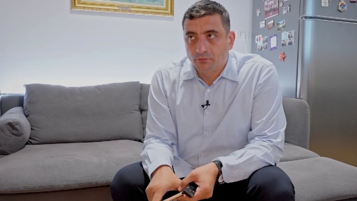 George Simion, în timp ce stă pe canapeaua din casa sa, îmbrăcat într-o cămașă albastră, cu telefonul în mână