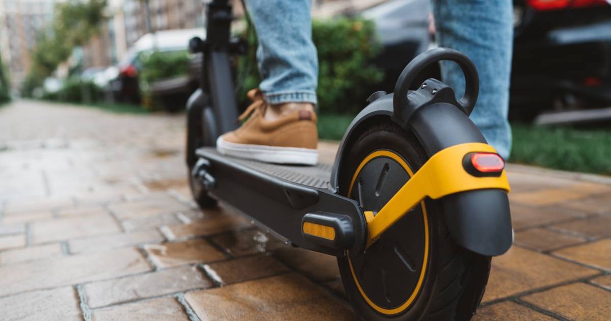 Un adolescent pe o trotinetă electrică, acesta are pantofi maro și blugi albaștrii